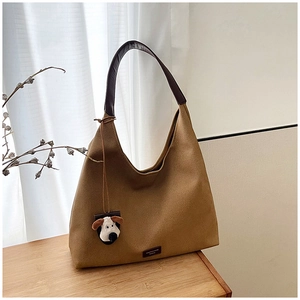 Brown suede tote bag with leather strap and a cute dog plush charm on a wooden table