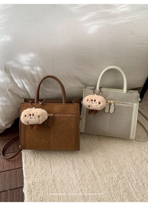 Detailed view of suede-like retro crossbody bags in dark brown and beige with plush charms