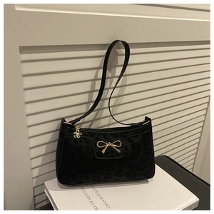 Detail of black leopard print shoulder bag with gold bow buckle on a white book