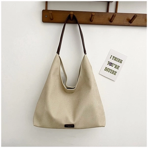Detail of a large textured canvas hobo bag with slim dark brown straps on a white wall