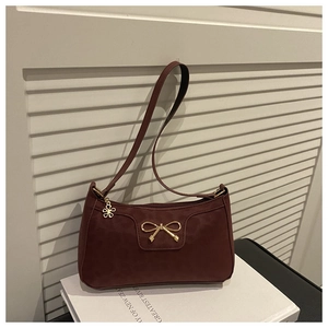 Close-up of a burgundy shoulder bag featuring a gold bow clasp and flower zipper charm