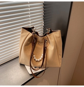 Detail of cream tote bag featuring pearl gold chain and leather straps in natural light