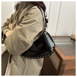 Détail d'un sac porté épaule noir avec rivets dorés assorti à un trench-coat classique