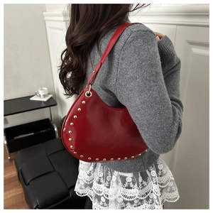 Vue détaillée du sac croissant rouge brillant avec rivets dorés porté sur un pull gris