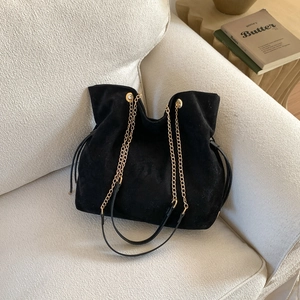 Retro black suede tote bag with golden chain strap on a white textured sofa