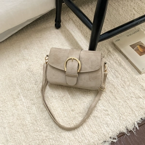 Close-up of beige oil-wax leather saddle bag with golden buckle on soft white rug