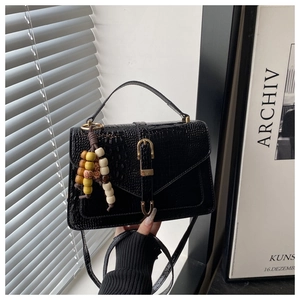 Detail of black crocodile pattern handbag with gold clasp and beaded charm