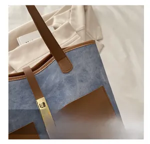 Detail of denim and brown leather tote bag featuring a gold metal twist lock closure