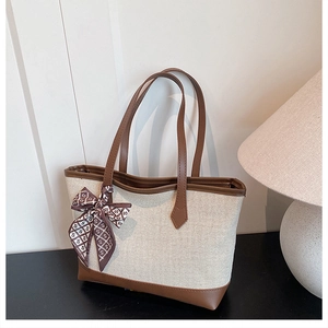 Close-up of beige canvas tote bag with brown leather trim and decorative silk scarf detail