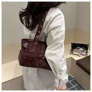 Detail of burgundy glossy leather shoulder bag with belt buckle on beige coat