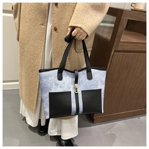 Detail of blue denim tote bag featuring black contrast pockets and gold metal buckle