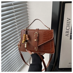 Detail of brown crocodile pattern handbag with leather buckle and beaded charm accessory
