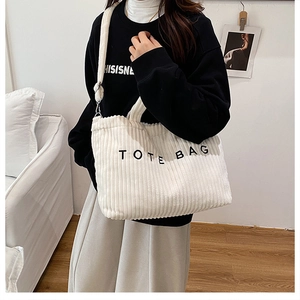Close-up of white corduroy tote bag with black letter print and adjustable shoulder strap