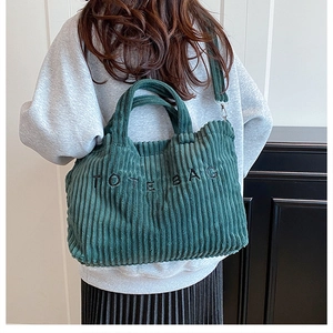 Green corduroy tote bag with TOTE BAG text shown on model for size and fit reference