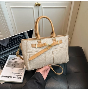 Close-up of structured beige canvas handbag with leather belts and golden hardware details