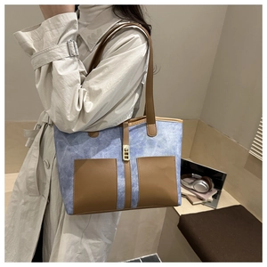 Detail view of a large blue and brown patchwork tote bag worn by a model in a cozy setting