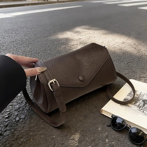 Deep brown textured leather crossbody bag with V-shaped envelope flap on street background