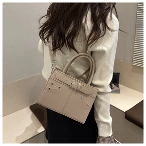 Detailed side view of a beige leather shoulder bag with buckle and rivet hardware