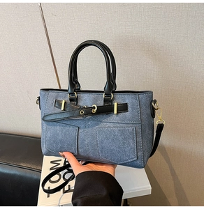 Detail of blue denim patchwork tote bag with black leather handles and gold buckles