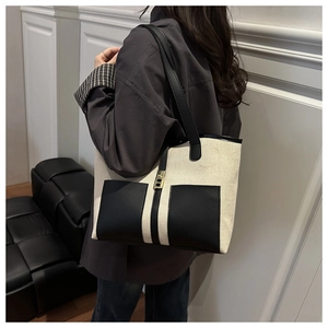 Close-up of a black and white canvas tote bag featuring leather pockets and gold lock
