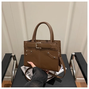 Detail of brown faux leather handbag with buckle accent and rivet trim on a black chair
