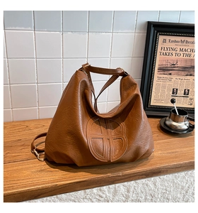 Detail of a large brown hobo tote bag featuring a unique circular stitched logo on soft leather