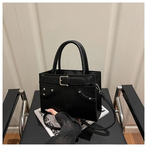 Detail of black leather tote bag with silver rivets and studs on a stylish surface