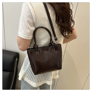 Détail latéral d'un sac seau marron foncé brillant avec bandoulière sur un mannequin