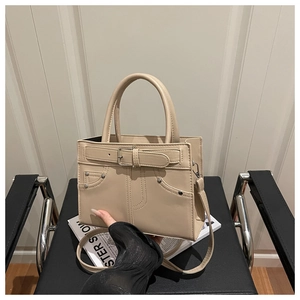 Detail view of cream tote bag with rivet accents and decorative buckle on a chair