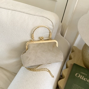 Beige suede shell bag with rich rabbit logo, gold metal handle and chain strap on a sofa