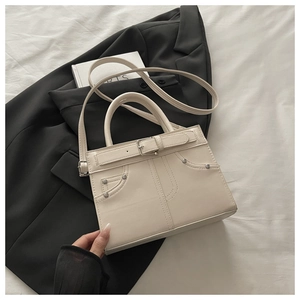 Detail view of cream square bag with decorative buckle and rivets on black blazer