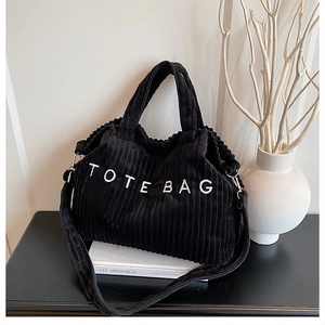 Close-up of black corduroy tote bag featuring white embroidered letters and a soft texture