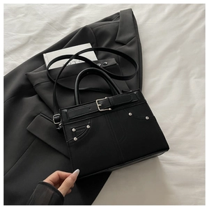Close-up of black crossbody bag featuring silver studs, belt buckle and matte leather texture