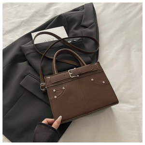 Close-up of brown faux leather handbag with buckle detail and rivets on a black blazer