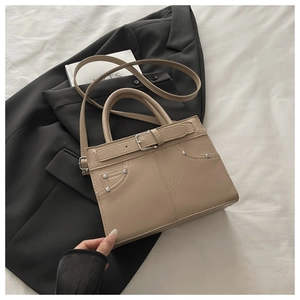 Detail of beige designer crossbody bag with rivet accents and pocket stitching detail