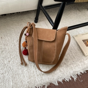 Détail du sac seau en daim marron avec breloques pompons colorés sur un tapis blanc