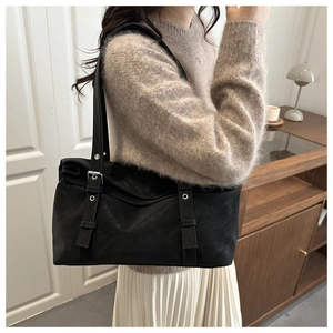 Detail of black suede shoulder bag with vertical straps and silver buckles on a model