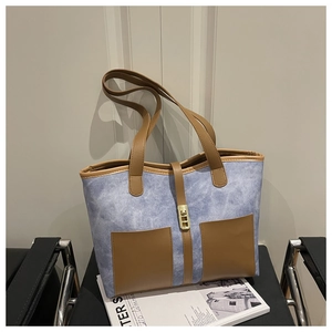 Detail of blue denim tote bag with brown leather pockets and gold metal buckle closure