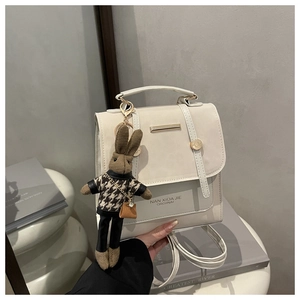Detail of a beige leather backpack with a gold bar accent and a cute bunny plush charm
