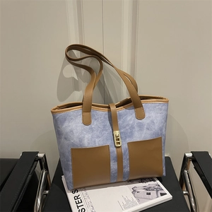 Retro blue denim tote bag with brown leather accents and gold lock on a chair