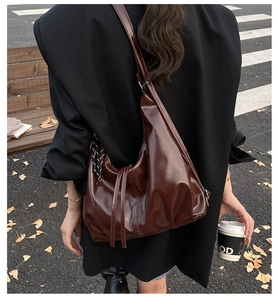 Detalle de bolso hobo marrón oscuro con acabado brillante y cordón decorativo