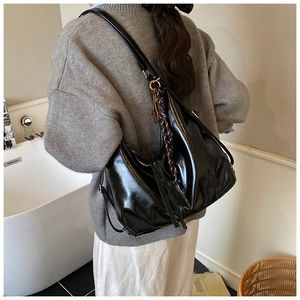 Detail of glossy black tote bag with silk scarf charm and adjustable metal buckle