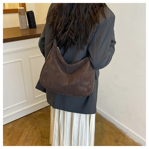 Detail of soft dark brown suede hobo bag worn over the shoulder by a model in a room