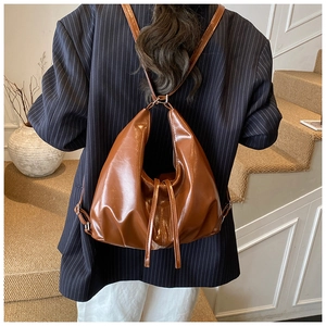 Brown glossy leather hobo bag shown in a backpack style on a striped blazer