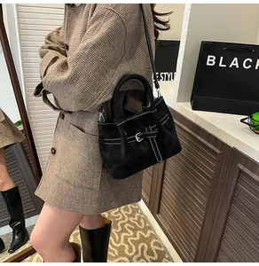 Detail of black suede-textured handbag with silver buckle and white contrast stitching