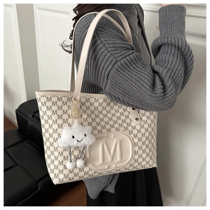 Detailed side view of beige large tote bag with M monogram and plush cloud pendant