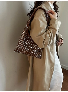 Sac seau marron avec rivets argentés porté par un mannequin en trench-coat beige
