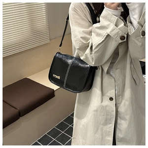 Detail of glossy black leather crossbody bag with white stitching and gold logo detail