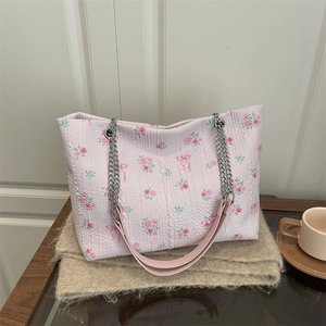 Pink floral tote bag with rose patterns and chain strap on soft cream plush background