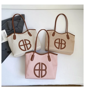 Flat lay of woven bucket bags in cream, brown, and pink with a leather HB logo patch